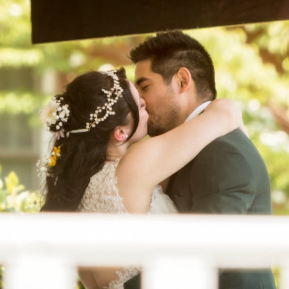 Romantic wedding kiss under a wooden pergola, bride in lace gown with pearl and floral hair accessories embracing groom in dark green suit, golden afternoon light filtering through leaves – timeless wedding photography by Imaginarium Pictures, West Michigan